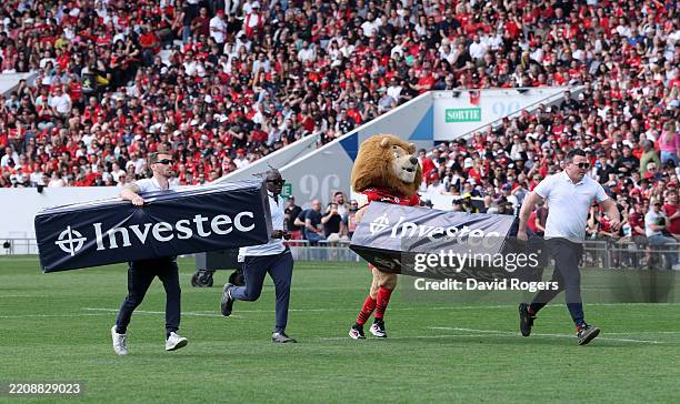 Stade Toulousain staff and club mascot Ovalion run across the pitch with post protectors after a parachutist delivering the match ball became caught...