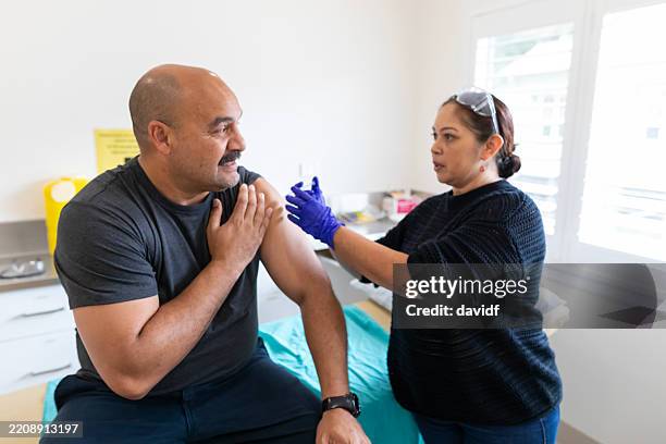pacific islander man receiving a vaccination injection from an australian aboriginal doctor - vaccination center stock pictures, royalty-free photos & images