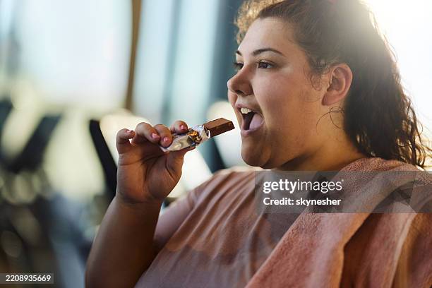 young overweight woman eating chocolate in a gym. - unhealthy living stock pictures, royalty-free photos & images