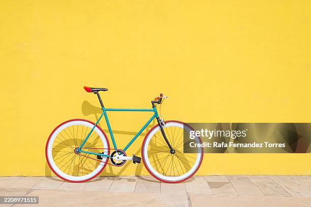 colorful bicycle leaning against a bright yellow wall. - fietsen stockfoto's en -beelden