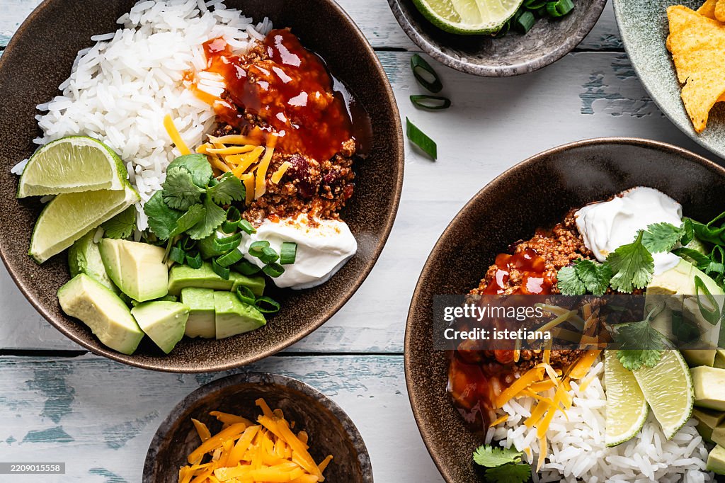 Chili con carne bowl with rice, avocado, cheese, cilantro, green onion, sour cream, and tortilla chips