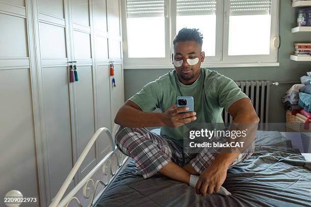 mann entspannt sich zu hause mit smartphone und trägt augenklappen - augenmaske stock-fotos und bilder