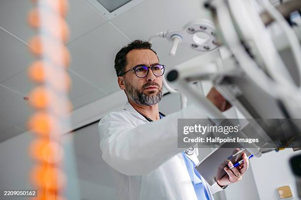 doctor in emergency room, looking at medical devices. - oncologist stock pictures, royalty-free photos & images