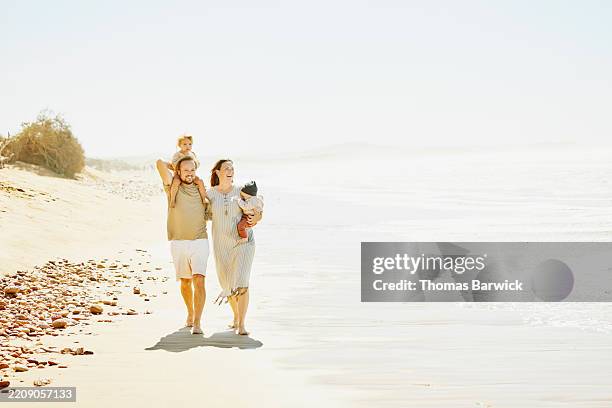 extreme wide shot mother and father carrying daughter and infant son on beach - older woman holding baby stock pictures, royalty-free photos & images