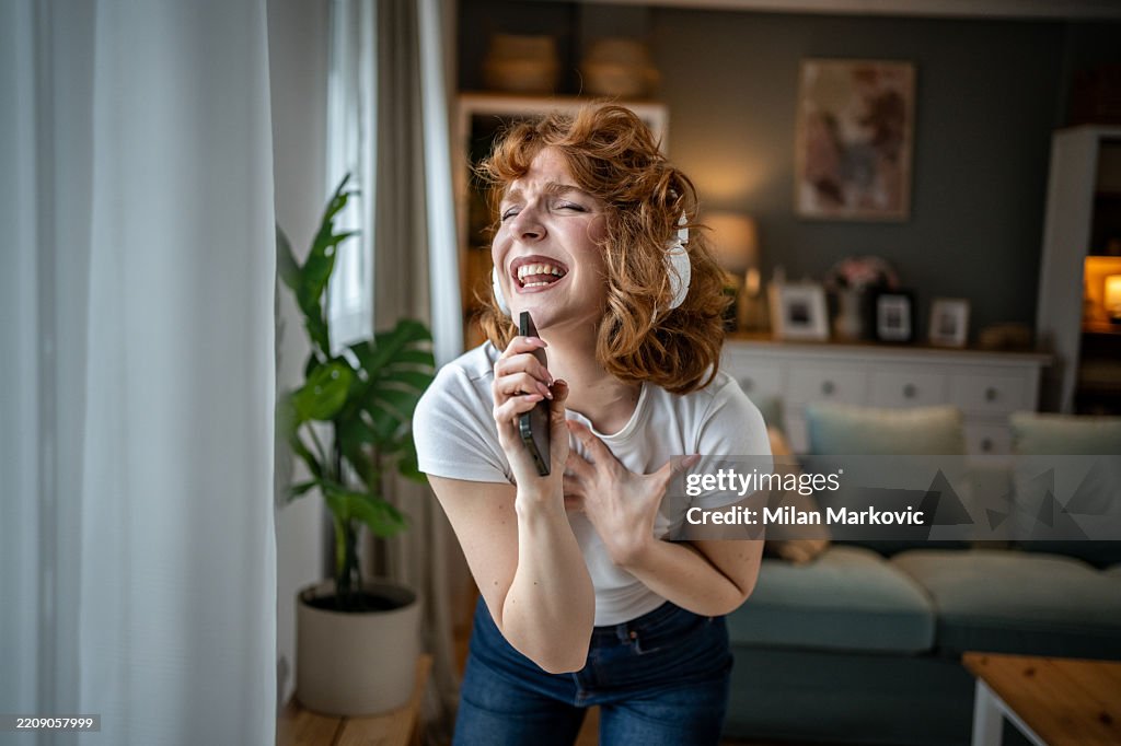 Young woman singing with headphones and smartphone at home