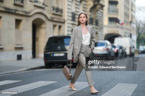 Diane Batoukina is seen wearing long straight brown hair, a beige Loro Piana oversized blazer, a white silk Loro Piana top with lace detailing, beige...