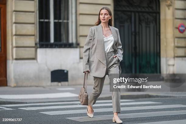 Diane Batoukina is seen wearing long straight brown hair, a beige Loro Piana oversized blazer, a white silk Loro Piana top with lace detailing, beige...