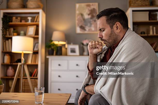 kranker mann hustet zu hause in decke gewickelt - krankenstand stock-fotos und bilder