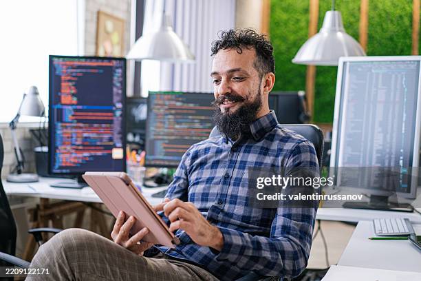 smiling it programmer using digital tablet. male specialist creating innovative software. engineer developing app, program, video game. writing code in terminal - video game programmer stock pictures, royalty-free photos & images