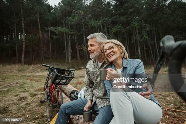 mature couple embracing while sitting on tree log - buitensport stockfoto's en -beelden