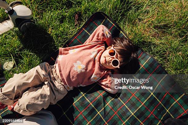 overhead shot of cute little girl with sunglasses lying down on picnic blanket - children only stock pictures, royalty-free photos & images
