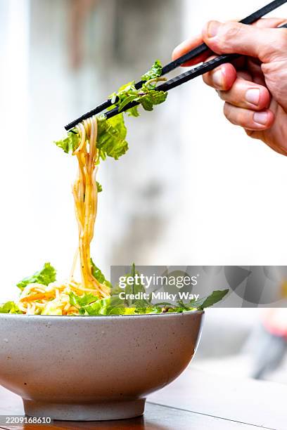 chopsticks lifting noodles and lettuce from a ceramic bowl. bright natural light with a soft background. - vietnamese coriander stock pictures, royalty-free photos & images