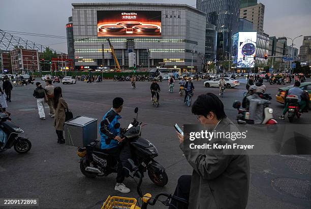 People wait to cross at a traffic light as a screen shows an ad for Apple's iPhone 16 on April 8, 2025 in Beijing, China. China announced plans...
