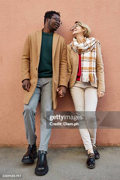 portrait of fashionable senior woman and young diverse man holding hands. - age contrast stock pictures, royalty-free photos & images