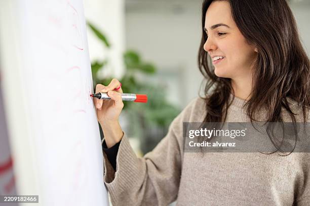 smiling young businesswoman writing on flipchart during meeting - flipchart stock pictures, royalty-free photos & images