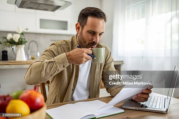focused man drinking coffee and reviewing documents while working from home - coffee testing stock pictures, royalty-free photos & images