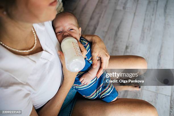 mother feeding her newborn baby son with milk from bottle while holding him in her arms - baby bottle stock pictures, royalty-free photos & images