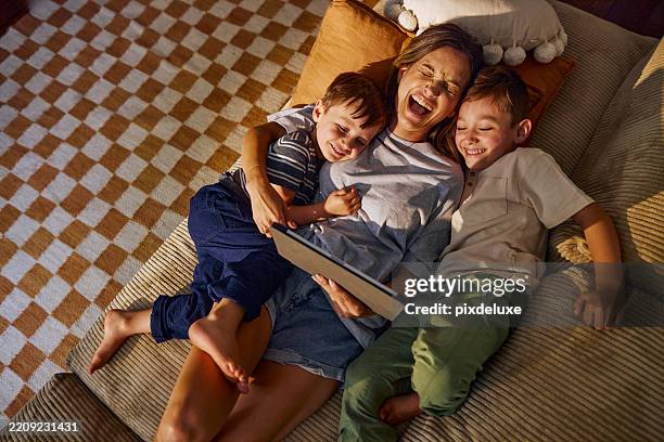 mutter liest mit ihren kindern auf dem sofa zu hause eine geschichte auf dem tablet vor - vier personen stock-fotos und bilder