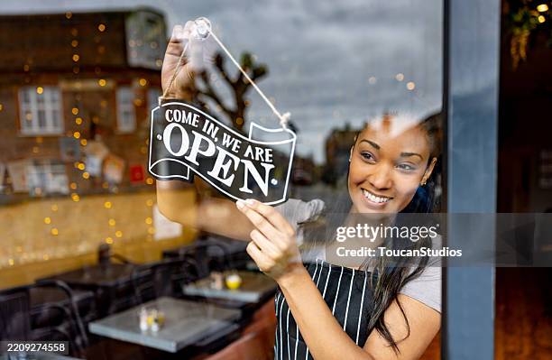 camarera colgando un cartel abierto en la puerta de una cafetería - señal de abierto fotografías e imágenes de stock