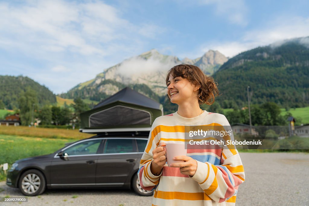 Woman drinking coffee in the camping during road trip with car with tent on the roof