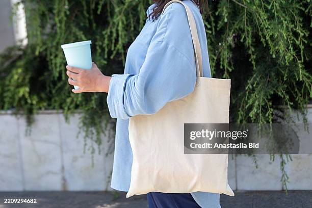 anonymous woman with cotton bag on the shoulder and reusable coffee cup in hands. - shopping bag stock pictures, royalty-free photos & images