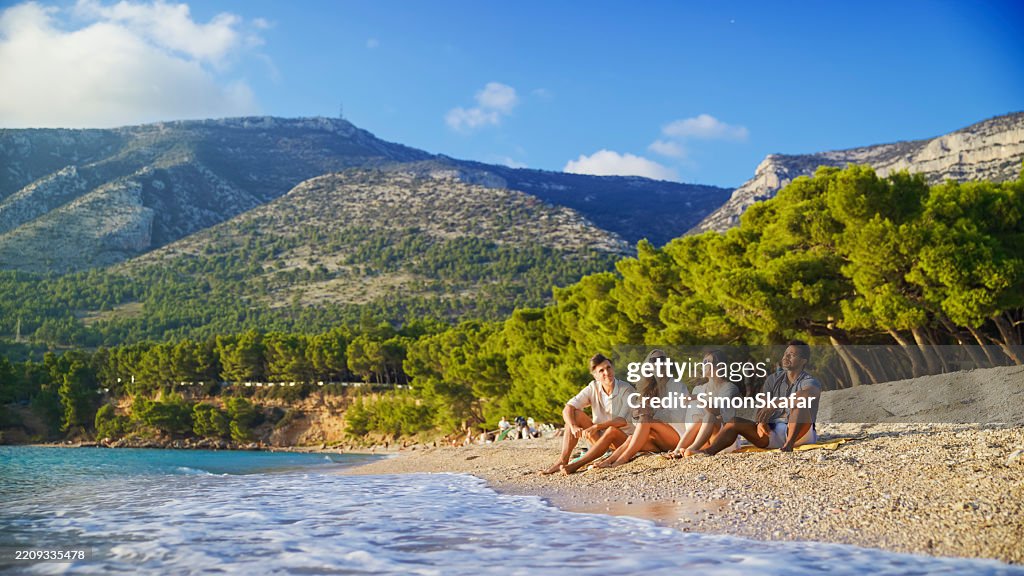 Diversos casais relaxando na praia de Zlatni Rat ao pôr do sol com cenário panorâmico de montanha