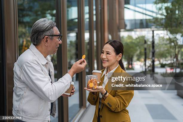 two senior colleagues enjoying snacks together during their coffee break - eet en drink gelegenheden stockfoto's en -beelden