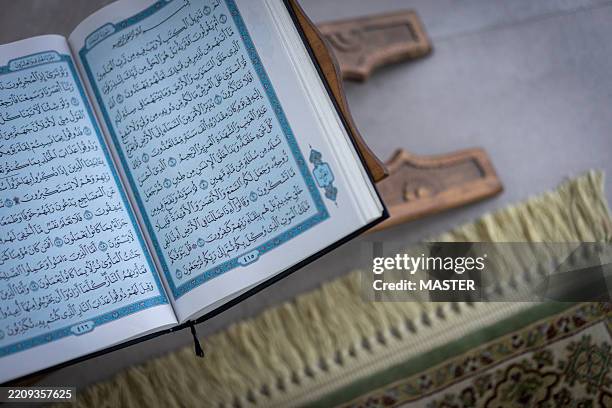 open quran on a wooden stand with a prayer mat beneath - coran photos et images de collection