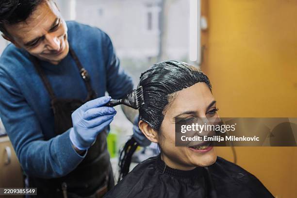 male hairdresser dyeing hair of the female client at the beauty salon. hairdresser applying and spreading hair color on woman's hair. small business hair salon. - ausmalen stock-fotos und bilder