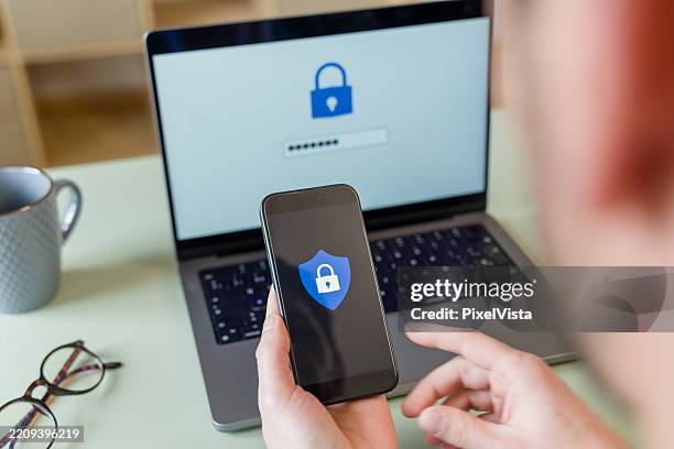 programmer securing data with two-factor authentication using laptop and smartphone - sob proteção imagens e fotografias de stock