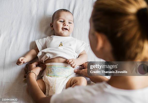 mother caring for baby while changing diaper at home - changing diaper stock pictures, royalty-free photos & images
