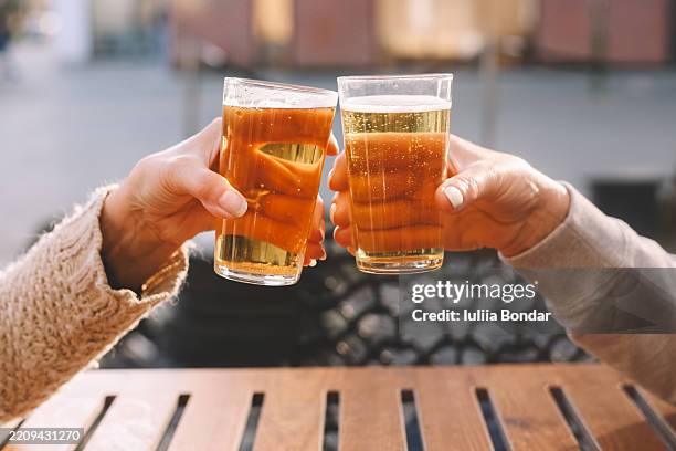 two people clinking beer glasses outdoors - toost stockfoto's en -beelden