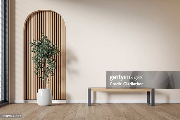 modern interior: an unfurnished living/waiting room with a modern bench, a potted plant (ficus) in front of a partly textured light beige (cream) neutral wall, partly arched paneled light pink wooden slat, large window and decoration - parket stockfoto's en -beelden