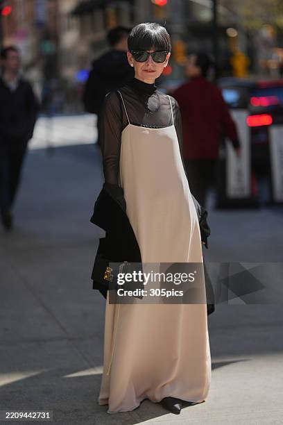 Lauren Levison is seen wearing black sunglasses, sheer black turtleneck, ivory slip dress, layered black necklace, oversized black coat draped over...