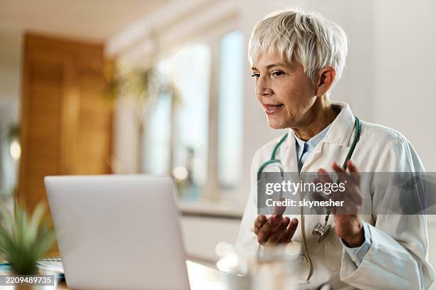 senior female doctor having a video call over laptop at her office. - werkende bejaarden stockfoto's en -beelden