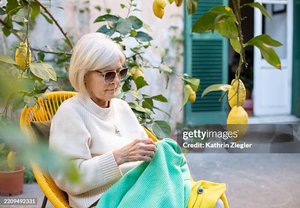 senior woman sitting in the garden, darning a cashmere sweater - knitted stock pictures, royalty-free photos & images