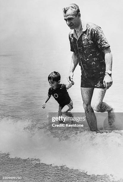 Shah Mohammed Reza Pahlavi of Iran, holding hands with his son, Crown Prince Reza, as they walk from the Caspian Sea towards the beach at Nowshahr,...