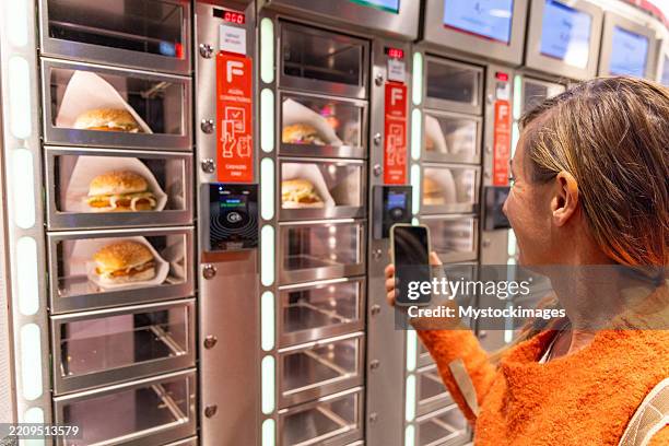 woman using automated food vending machine while smiling - vending machine stock pictures, royalty-free photos & images