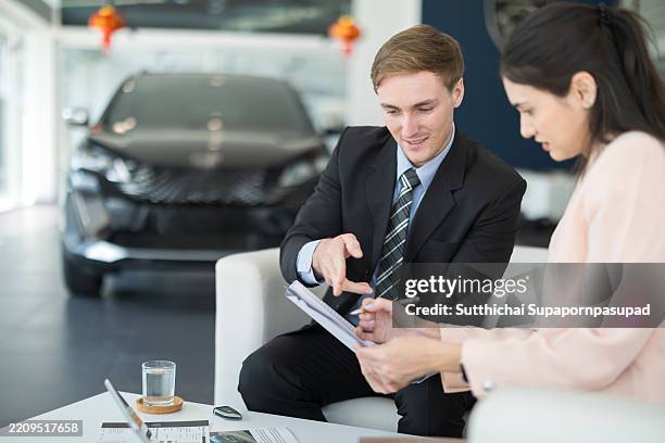 male car dealer engaging with a potential customer inside a modern car showroom, discussing vehicle features and sales options during a business conversation about purchasing a new car - autokredit stock-fotos und bilder