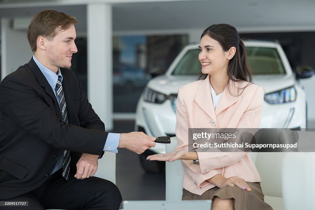 Male car dealer hands over car key to happy customer in modern showroom during daytime, symbolizing successful car purchase, great customer service, and vehicle handover experience