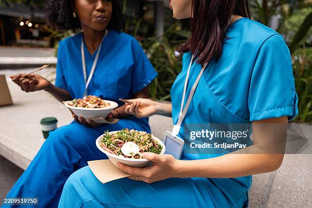 healthcare professionals enjoying a break with healthy meals outdoors in uniform - lunchpauze stockfoto's en -beelden