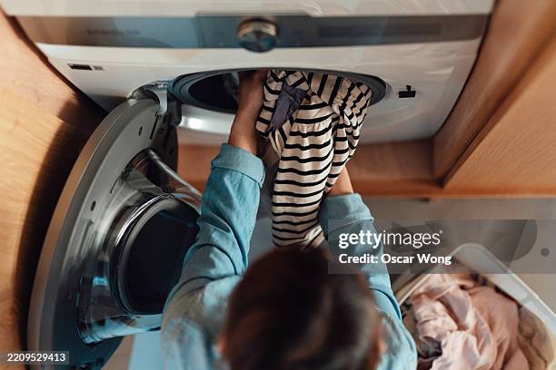overhead view of young asian woman loading the washing machine with laundry - launderette stock pictures, royalty-free photos & images