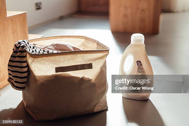 a laundry basket filled with dirty laundry and a bottle of liquid detergent - lessive photos et images de collection