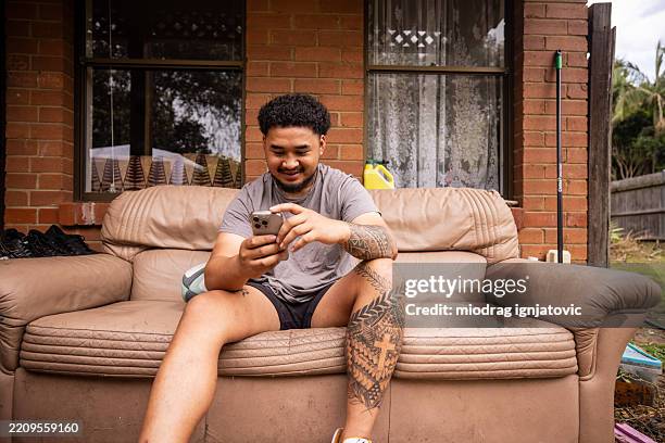jeune homme vérifiant son téléphone - tatouage polynésien photos et images de collection