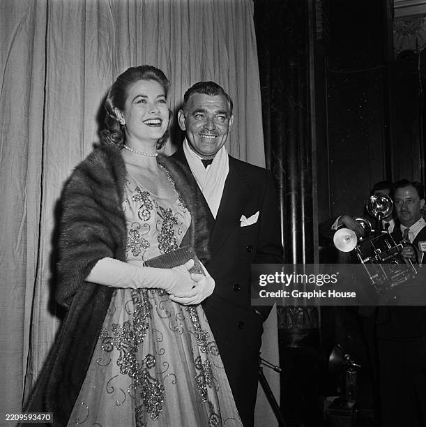 American actress Grace Kelly, wearing a fur coat over an embroidered evening gown with evening gloves, and American actor Clark Gable, who wears an...