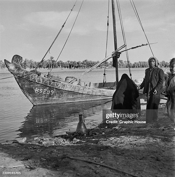 Sailboat at the river's edge as an Iraqi man stands on a Shatt al-Arab riverbank in Al-Qurnah, Iraq, 13th November 1955. Located northwest of Basra,...