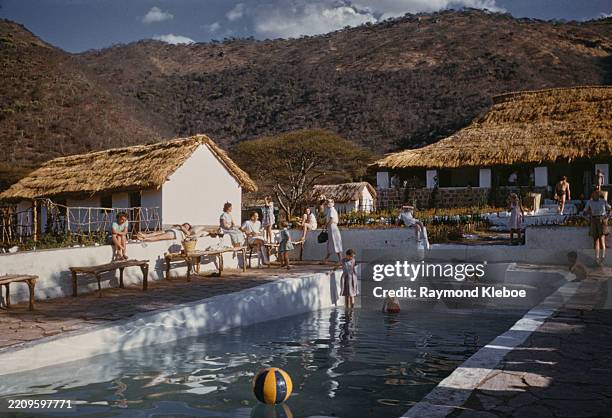 People relaxing at the poolside, with thatched buildings in the background, East Africa, circa 1955.