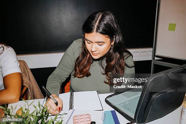 young woman writing on diary while sitting with laptop in classroom at university - flash stock pictures, royalty-free photos & images