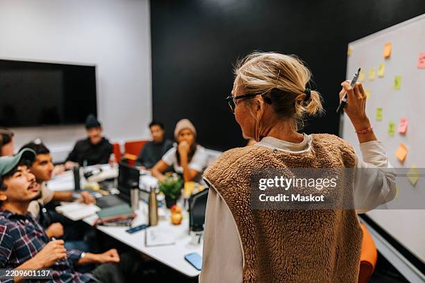 rear view of female teacher holding felt tip pen teaching multiracial students in classroom at college - technical college stock pictures, royalty-free photos & images