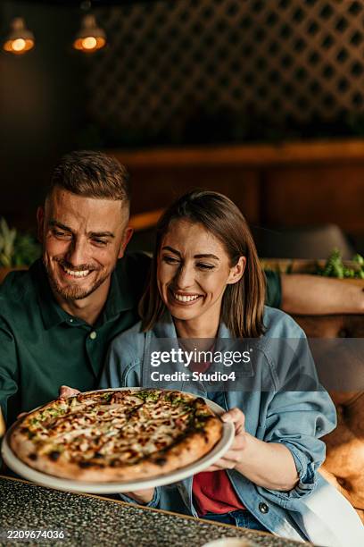 happy couple showing delicious pizza in a restaurant - pizzeria stock pictures, royalty-free photos & images